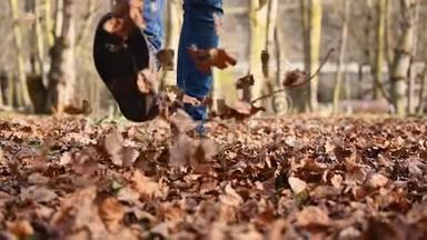 秋天在田园诗般的公园里散步时，嬉戏的人踢起一堆五颜六色的叶子。 走在路上的人